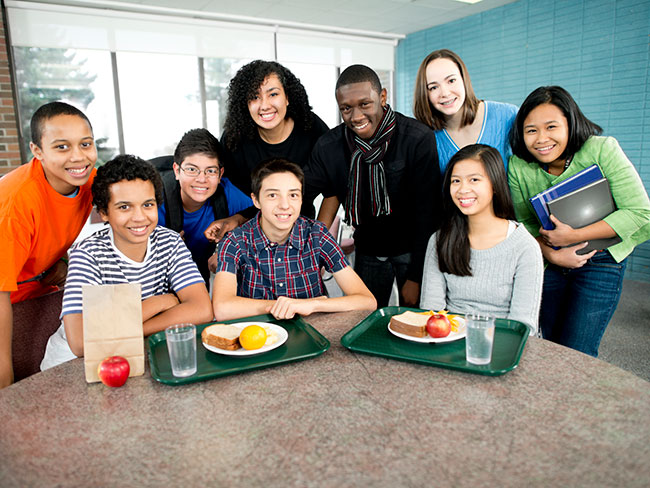 Diverse group of kids gathered around a table for school lunch